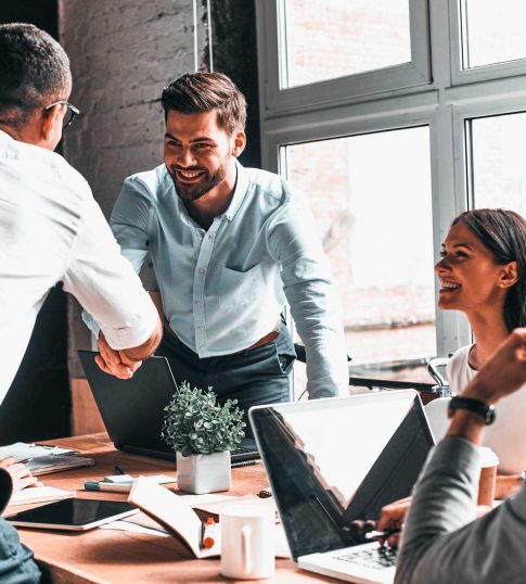 Young modern men in smart casual wear shaking hands and smiling while working in the creative office